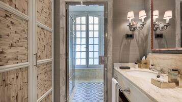 A bathroom with a glass shower door, a sink with a marble countertop, and a mirror with wall sconces.
