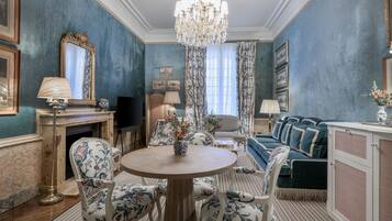 A room with a round wooden table surrounded by floral-patterned chairs, a blue sofa, a chandelier, and a fireplace.