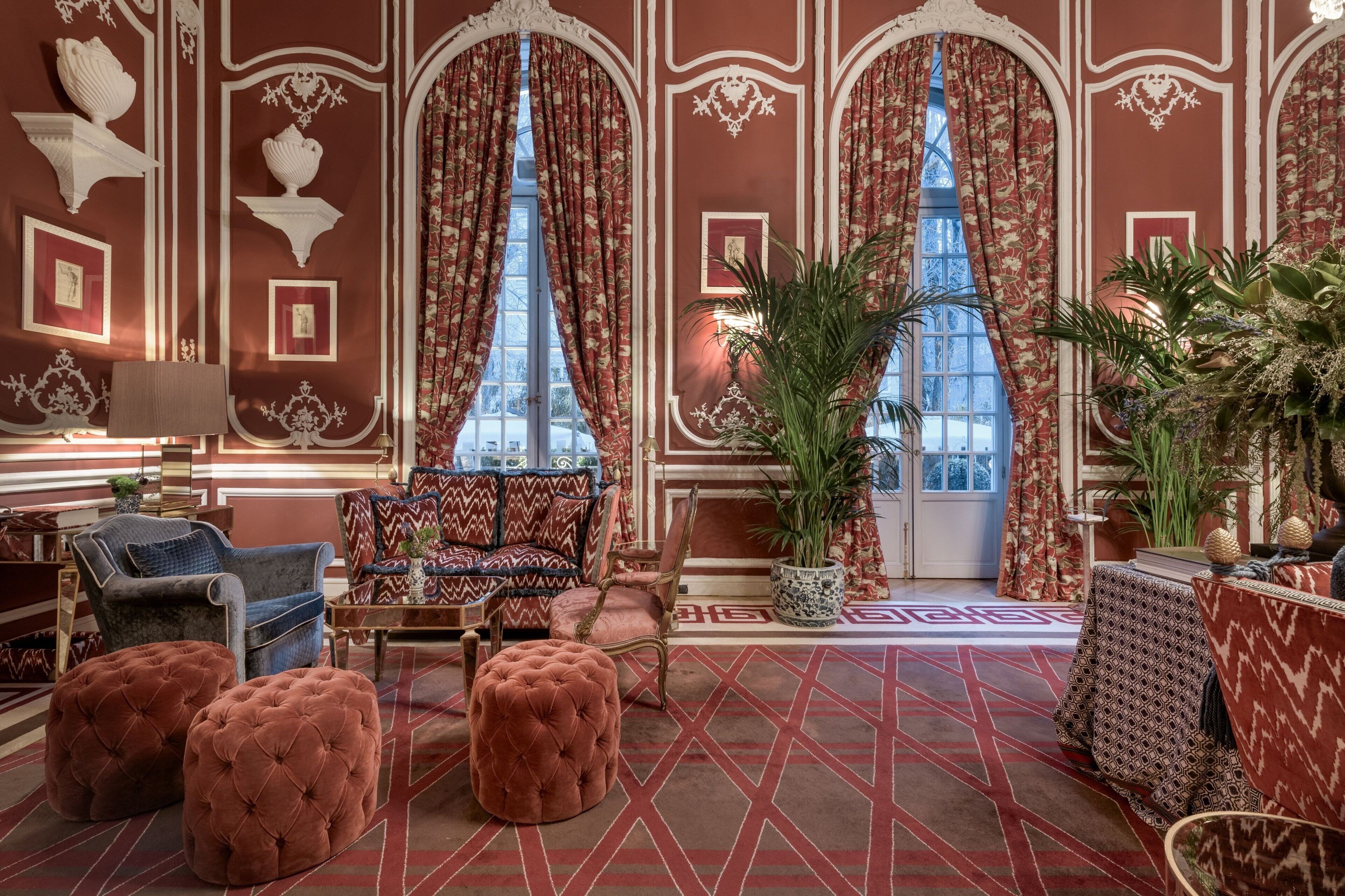A room with a patterned carpet, a sofa set, a blue armchair, and a large potted plant.