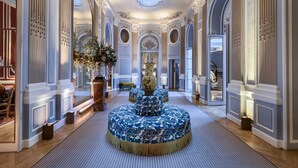 Um hall imponente com colunas decoradas, uma fonte central ornamental e uma escadaria que leva a um andar superior.