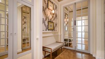 Un couloir avec un banc, une porte double dotée de panneaux de verre et un papier peint à motifs.