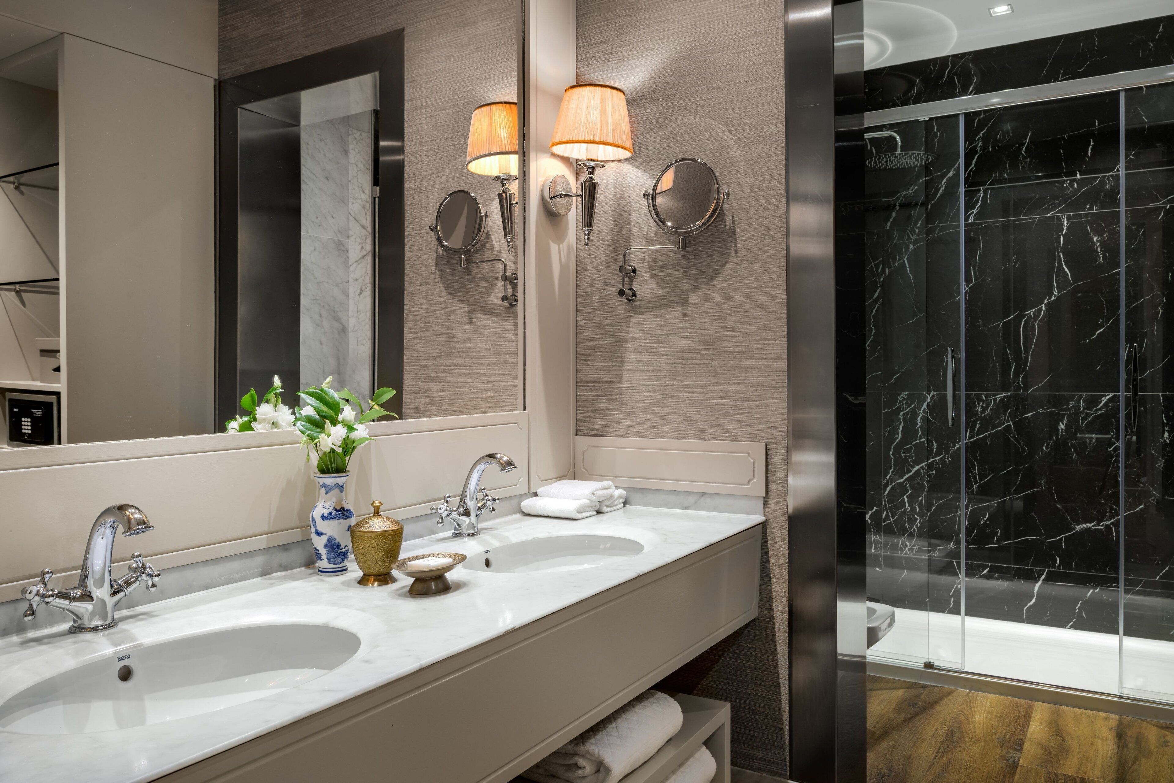 Un baño moderno con dos lavamanos, un espejo grande, luces empotradas en la pared y una zona de ducha con azulejos de mármol.