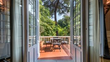 An open door leading to a patio with a table and chairs, surrounded by greenery and a view of trees.