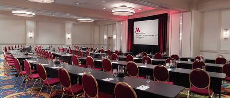 Una sala conferenze con lunghe tavolate, sedie rosse e un grande schermo che mostra il logo Marriott.