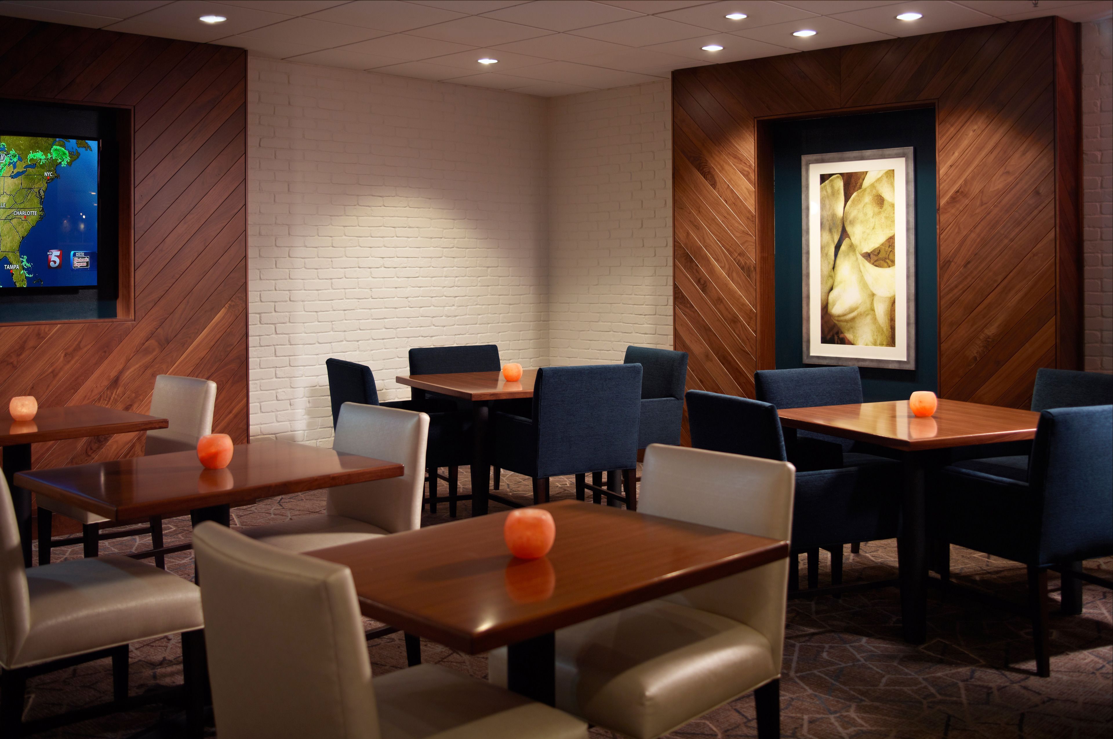 A hotel room with a large TV displaying a weather forecast, a wooden accent wall, and a framed artwork.