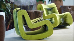 A uniquely designed green chair with a curved structure, placed in a room with a large window and potted plants. - Atlanta Marriott Northwest at Galleria (Atlanta)