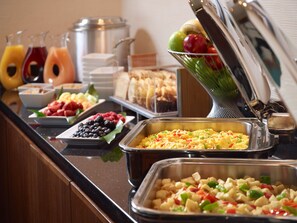 Un bufé con diversas opciones de comida, incluyendo frutas, verduras y platos ya preparados.