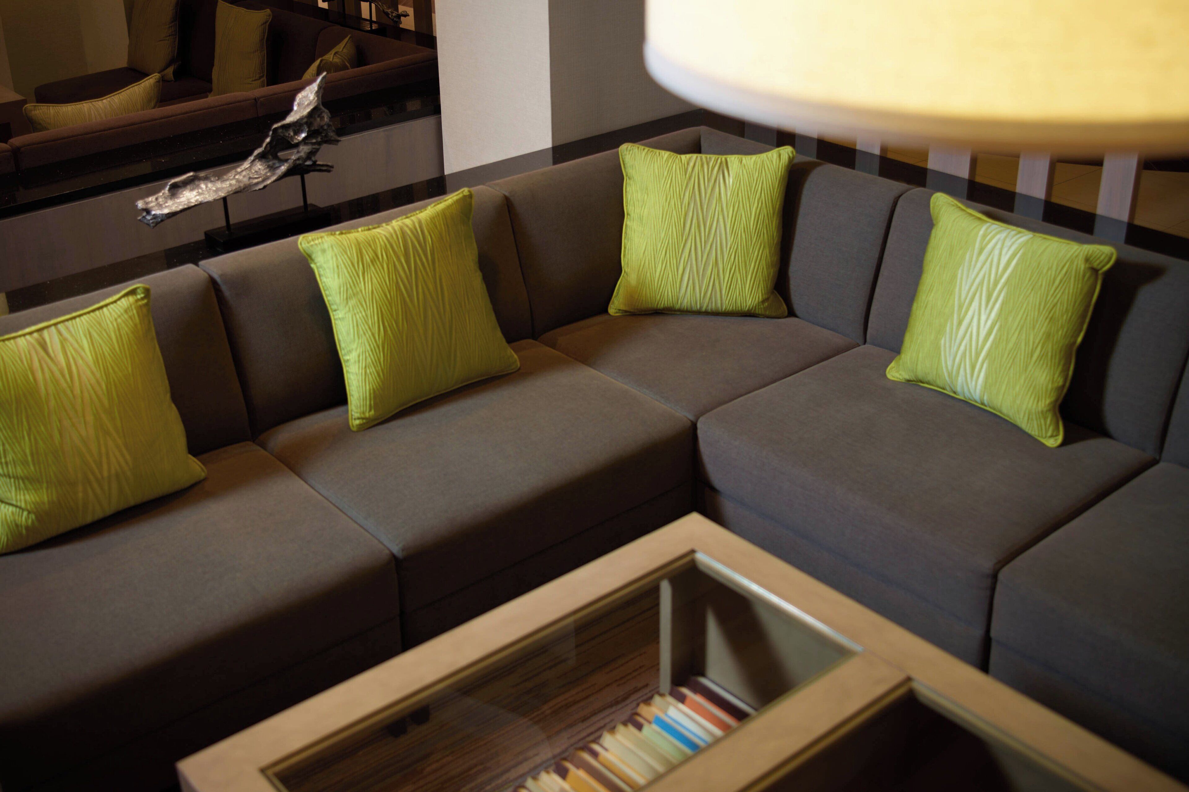 A modern living room with a sectional sofa, green cushions, and a glass coffee table.