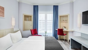 A hotel room with a bed, two red chairs, a desk, a TV, and a window with blue curtains. - IntercityHotel Hamburg-Altona (Hamburg)