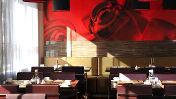 A restaurant with tables and chairs, a large red mural on the wall, and black pendant lights.