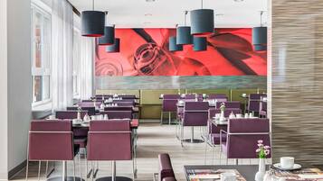 A modern dining area with purple chairs and tables, a large red mural on the wall, and pendant lighting.