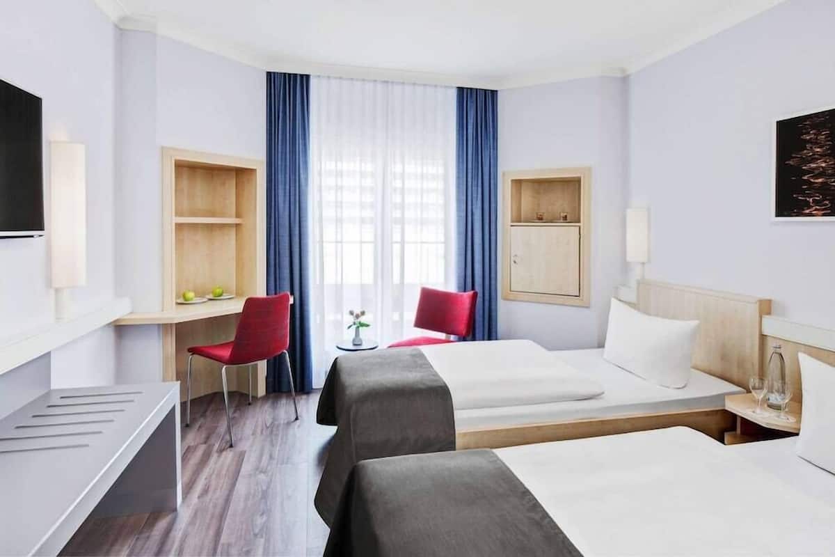 Habitació d'hotel amb dos llits, una taula, una cadira i un televisor.