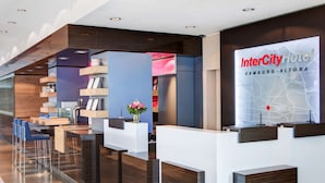 A modern hotel reception area with a reception desk, bar seating, and a large digital display advertising the InterCity Hotel in Hamburg-Altona. - IntercityHotel Hamburg-Altona (Hamburg)