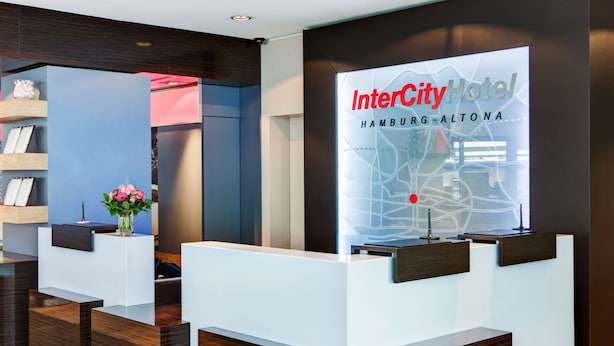 A reception area with a digital display of the InterCity Hotel in Hamburg-Altona, featuring a modern design with wooden accents and a vase of flowers. - IntercityHotel Hamburg-Altona (Hamburg)
