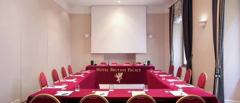 Un salón de conferencias con una larga mesa, sillas rojas y un cartel que dice 'Hotel Brufani Palace'.