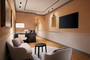 A hotel room with a sofa, a small round table, a desk with a lamp, a flat-screen TV, and a mirror on the wall. - Sina Brufani (Perugia)