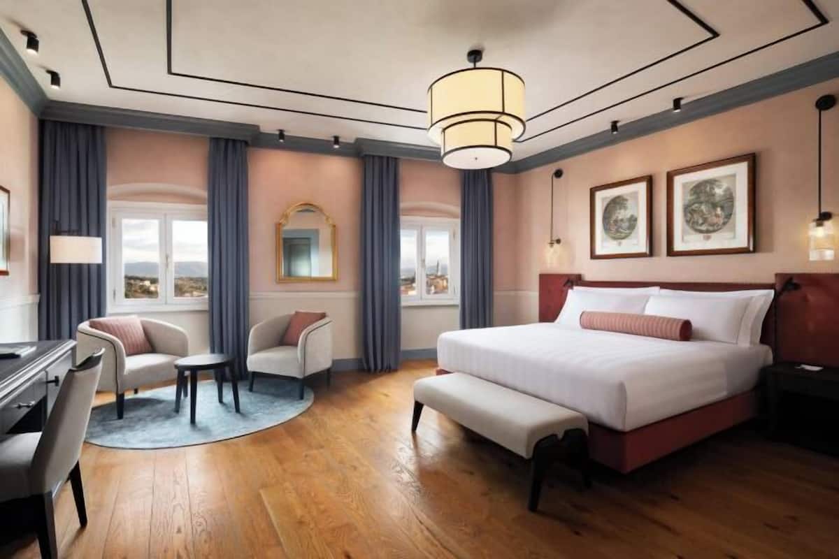 A hotel room with a bed, a desk, a chair, a round table, and a view of the city.