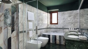 Ein modernes Badezimmer mit einer gläsernen Duschkabine, zwei weißen Bidets, einem weißen Waschbecken und einer Wand mit Marmorfliesen.