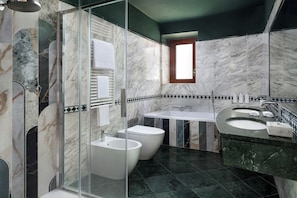 Un baño moderno con ducha envuelta en vidrio, dos bidés blancos, un lavabo blanco y un revestimiento de mármol en la pared.