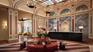 A lobby with a red sofa, round tables, a reception desk, and a mural. - Sina Brufani (Perugia)