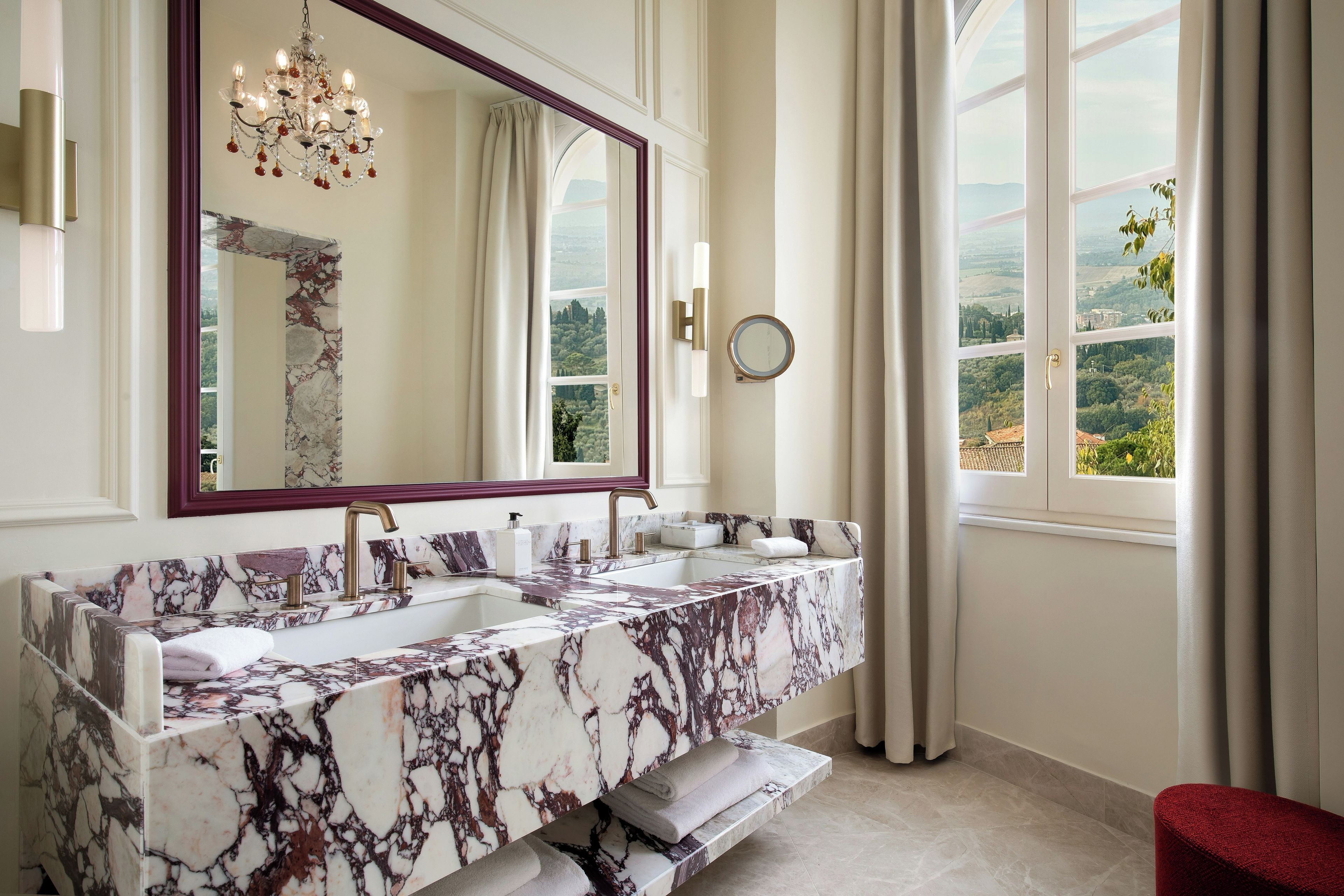 Un bagno con un vanità in marmo, uno specchio grande, un lampadario e vista sul paesaggio.