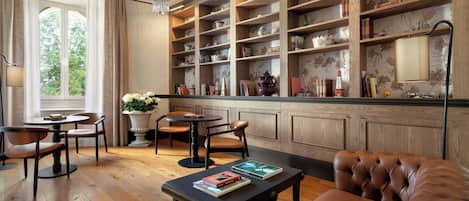 Eine Bibliothek mit Bücherregalen, einer Kandelaber, einem Tisch mit Stühlen und einem Ledersofa.