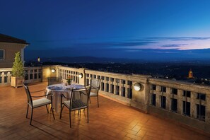 A terrace with a table and chairs, a railing, and a view of a cityscape at dusk. - Sina Brufani (Perugia)