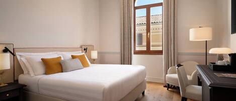 Une chambre d’hôtel avec un lit, un bureau, une chaise, une lampe et une fenêtre avec des rideaux.