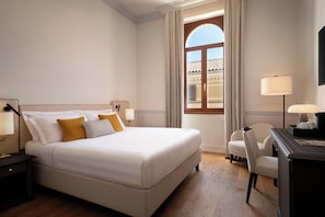 A hotel room with a bed, a desk, a chair, a lamp, and a window with curtains.