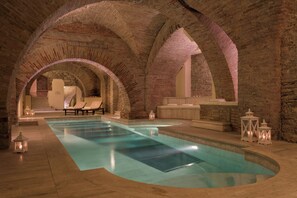 Una piscina interior con techos de ladrillo abovedados, sillones de descanso y faroles decorativos.