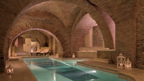 An indoor swimming pool with arched brick ceilings, lounge chairs, and decorative lanterns. - Sina Brufani (Perugia)