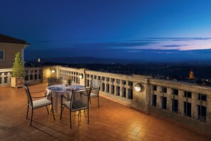 Une terrasse avec une table et des chaises, une balustrade et une vue sur le paysage urbain au crépuscule.