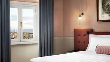 Une chambre d’hôtel avec un lit, une vue par la fenêtre, une tête de lit capitonnée et un tableau encadré au mur.
