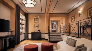 A modern living room with a sofa, ottomans, a flat-screen TV, a fireplace, and a staircase leading to another level. - Sina Brufani (Perugia)