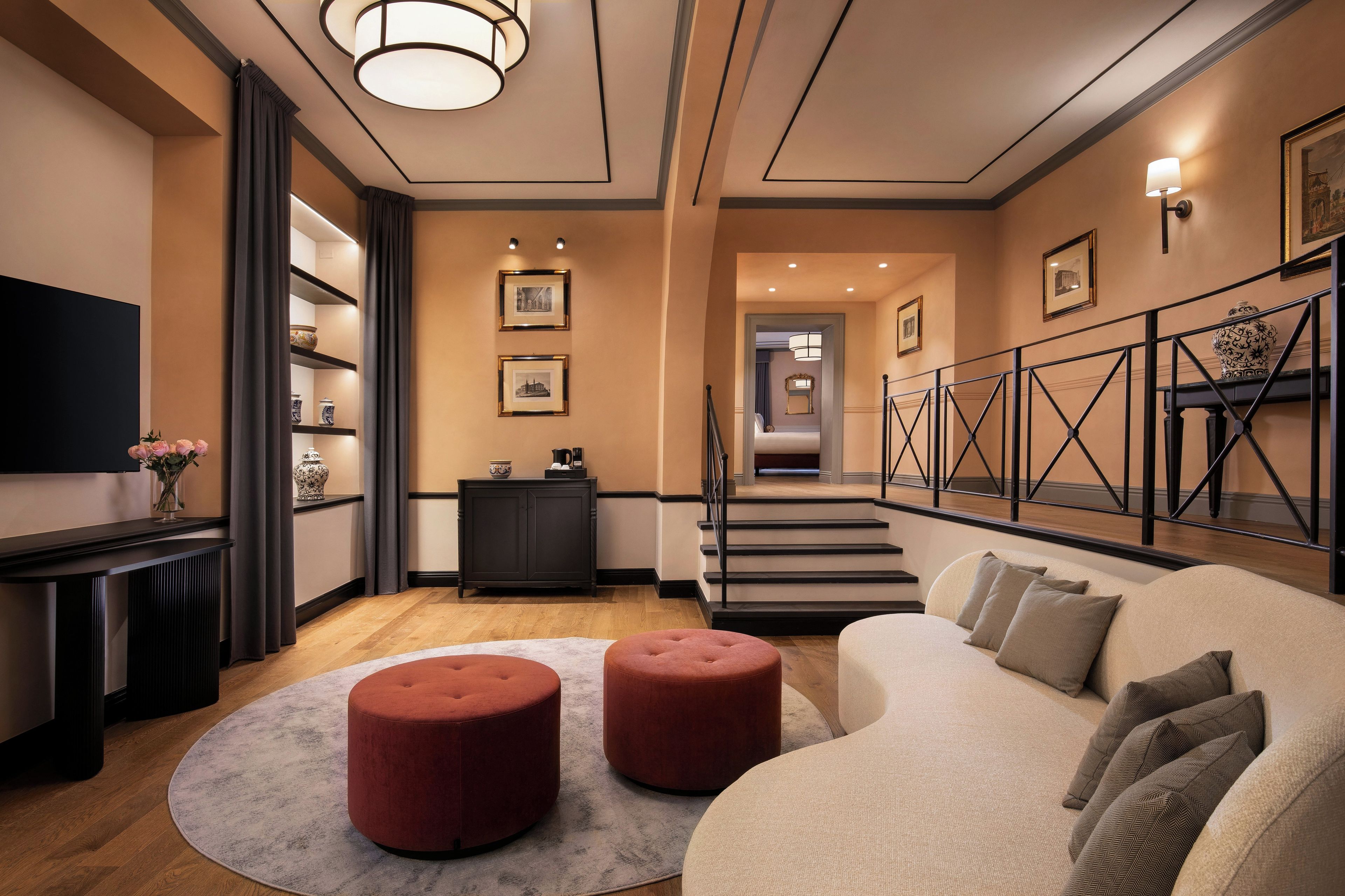 Un salon moderne comprenant un canapé, des poufs, un téléviseur à écran plat, une cheminée et un escalier menant à un autre niveau.