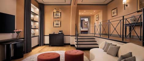 A modern living room with a sofa, ottomans, a flat-screen TV, a fireplace, and a staircase leading to another level.