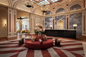 A lobby with a red sofa, round tables, a reception desk, and a mural. - Sina Brufani (Perugia)