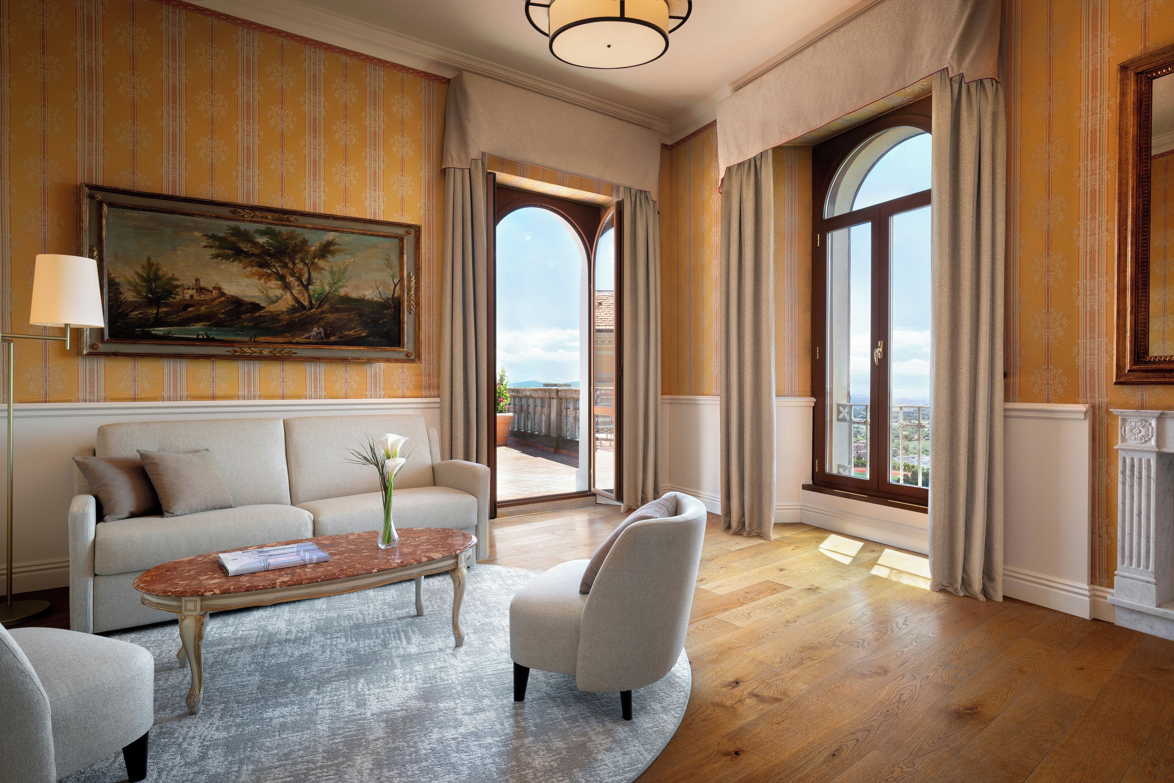 A spacious living room with a sofa, armchair, coffee table, and a large painting on the wall.