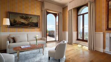 A spacious living room with a sofa, armchair, coffee table, and a large painting on the wall.