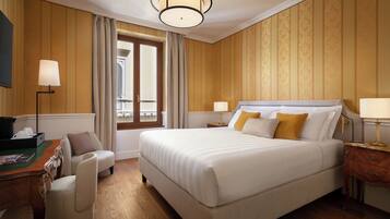 A hotel room with a large bed, a desk with a chair, a lamp, and a window with curtains.