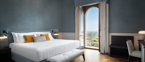 A bedroom with a large bed, a bench, a desk, and a view through a window.