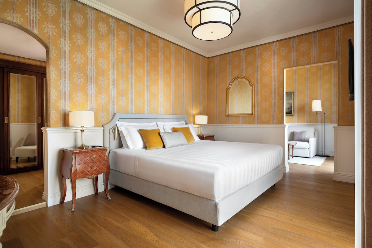 A hotel room with a large bed, a nightstand, a chair, a desk, and a mirror.