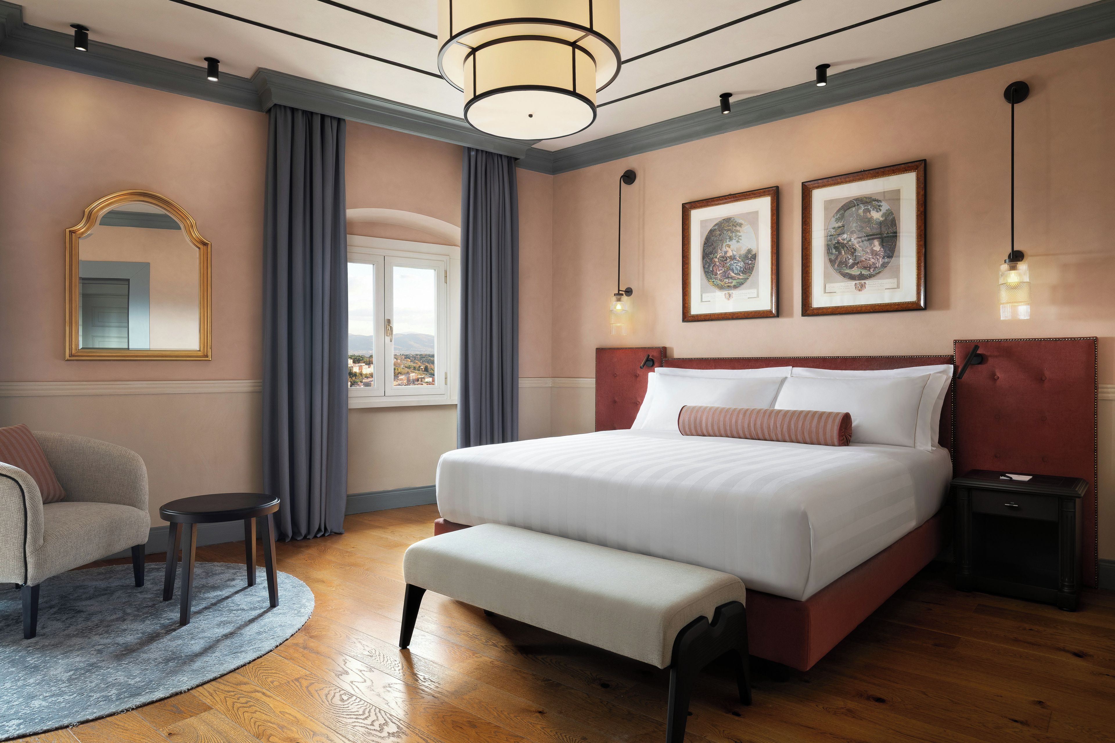Ein Schlafzimmer mit einem großen Bett, einem Sessel, einem kleinen Tisch und zwei gerahmten Bildern an der Wand.