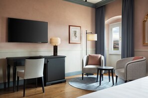 A hotel room with a flat-screen TV, a desk with a chair, a sofa, a small table, and a lamp.
