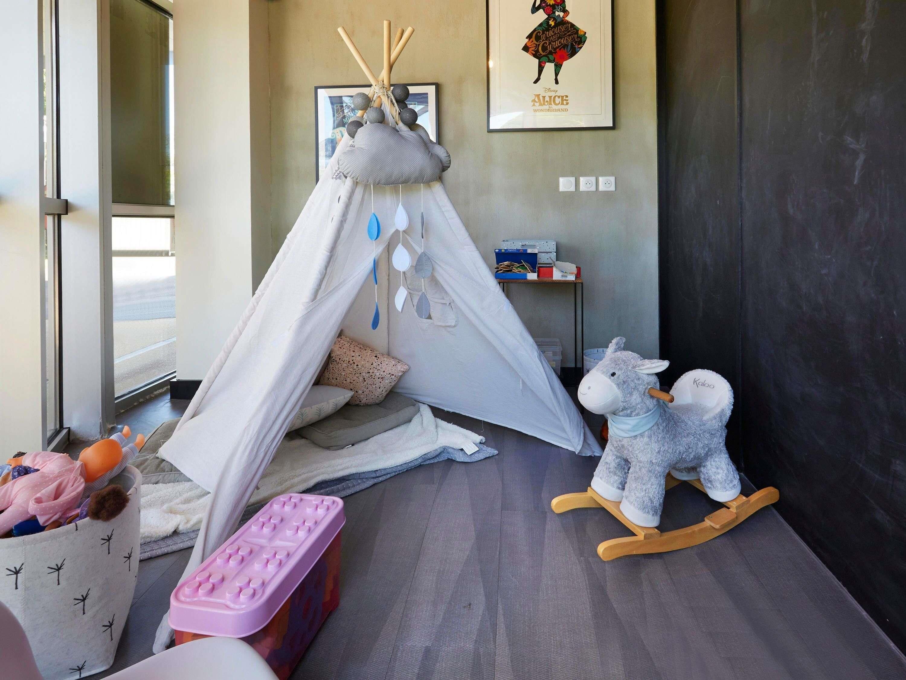 A child's play area with a teepee, a rocking horse, and a storage bin.