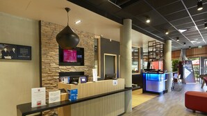 A reception area with a wooden reception desk, a stone wall, a mounted TV, and a punching bag. - ibis Archamps Porte de Geneve (Archamps)