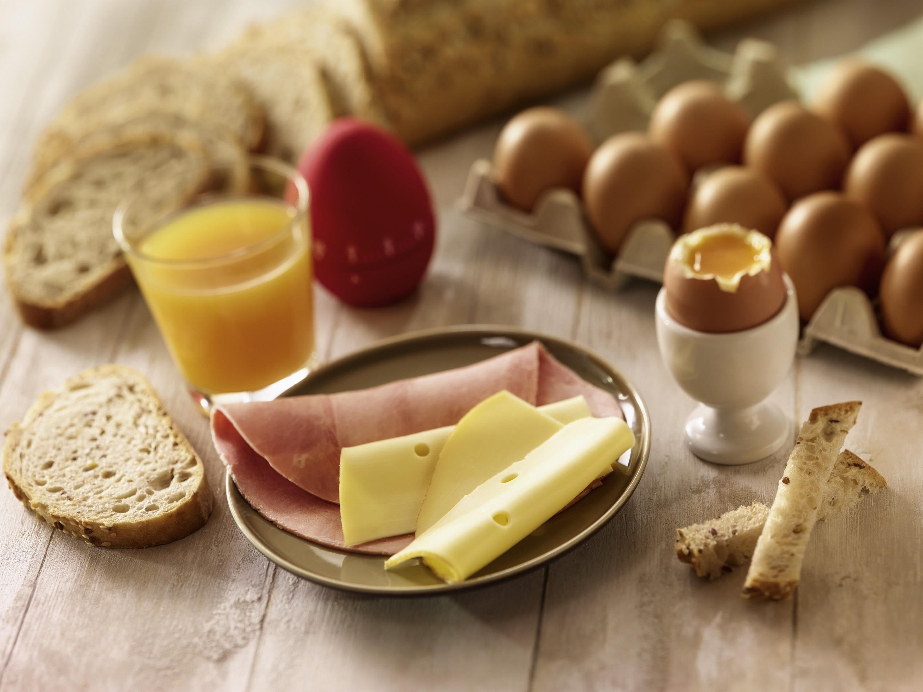 Een ontbijttafel met brood, eieren, kaas en een glas sinaasappelsap.