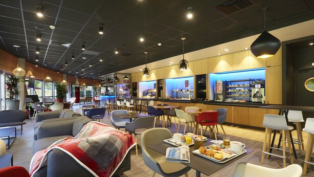A modern cafe with seating areas, a bar, and a breakfast setup. - ibis Archamps Porte de Geneve (Archamps)