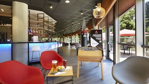 A modern bar area with seating, a foosball table, and a view of the outdoors. - ibis Archamps Porte de Geneve (Archamps)