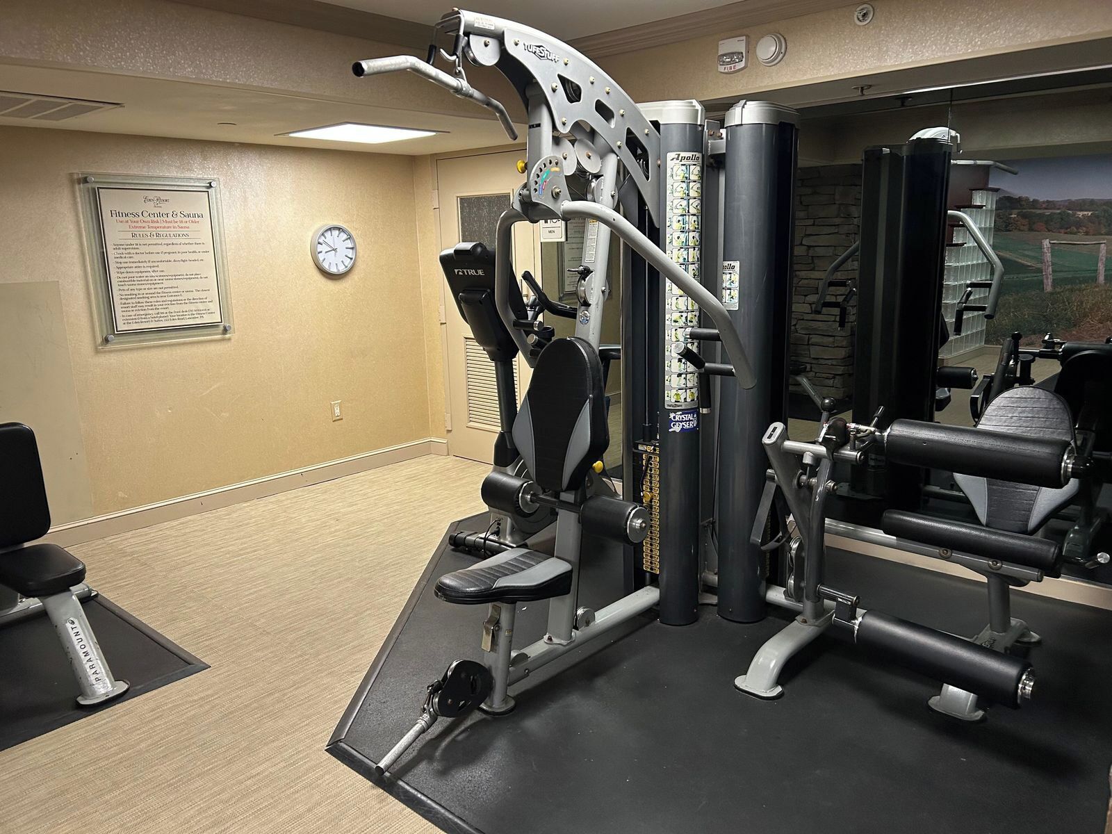 A fitness center with exercise machines, a clock, and a sauna sign on the wall.